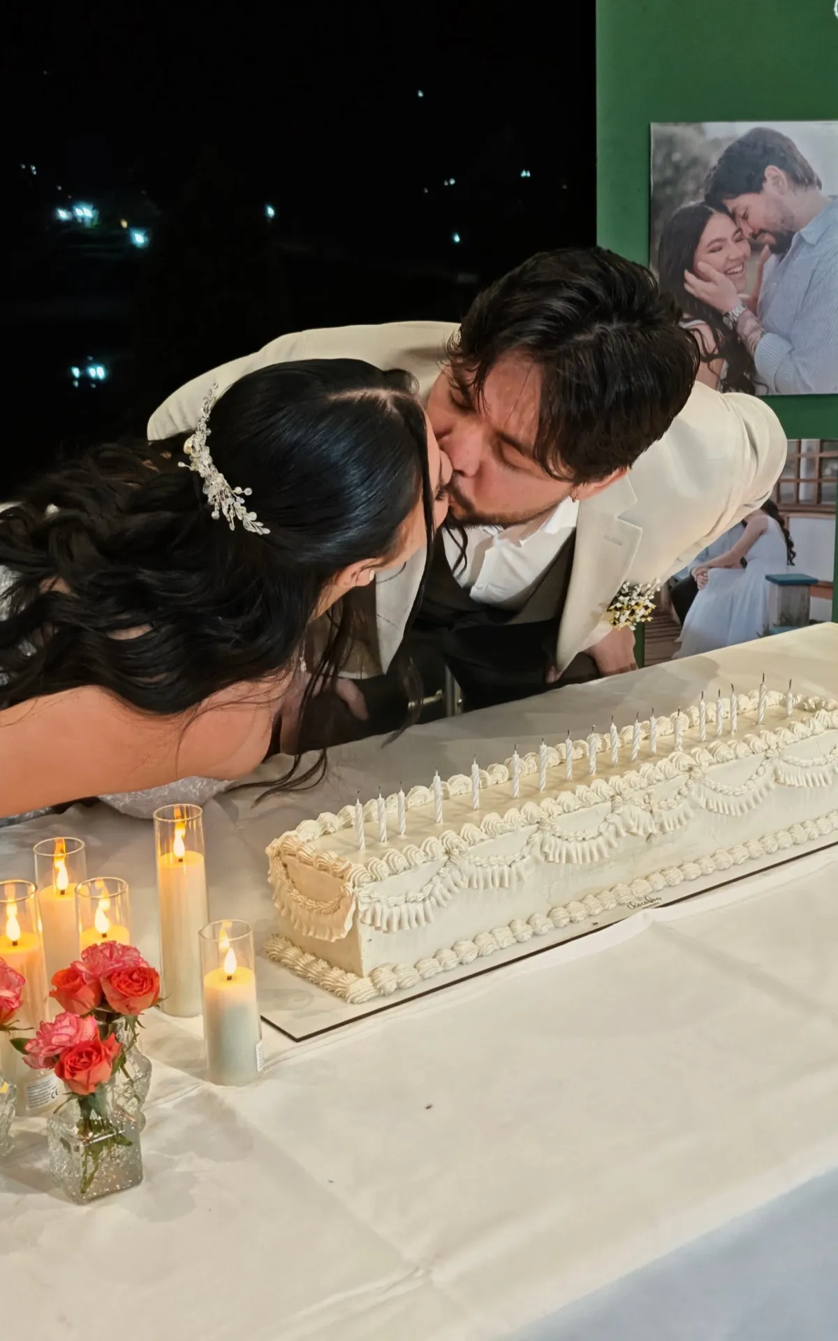 Novios besándose sobre torta de bodas alargada con velas encendidas en el centro — Chocobon Bucaramanga