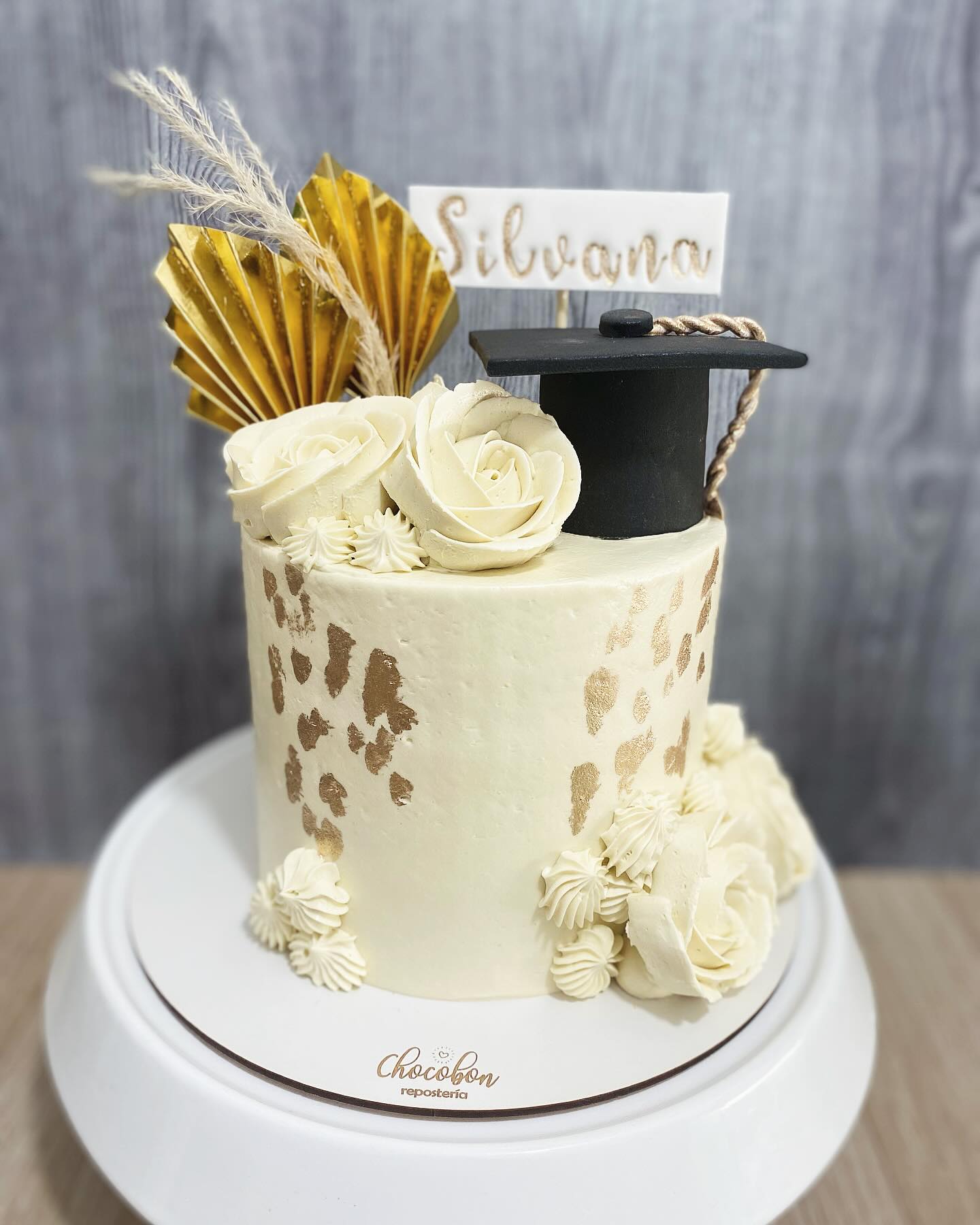 Torta de grado en marfil con pinceladas de pan de oro, rosas de buttercream, abanico dorado y birrete negro