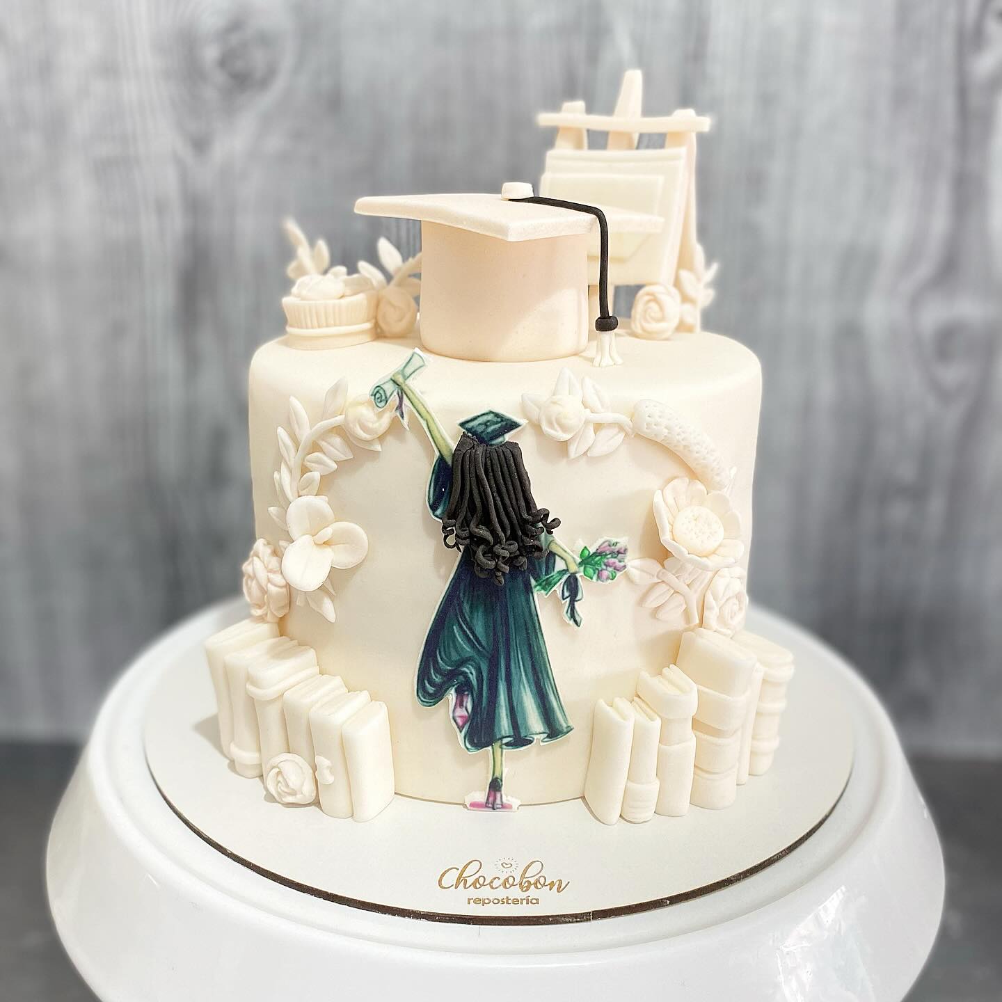 Torta de grado con silueta de graduada modelada a mano, diploma, birrete y libros en azúcar